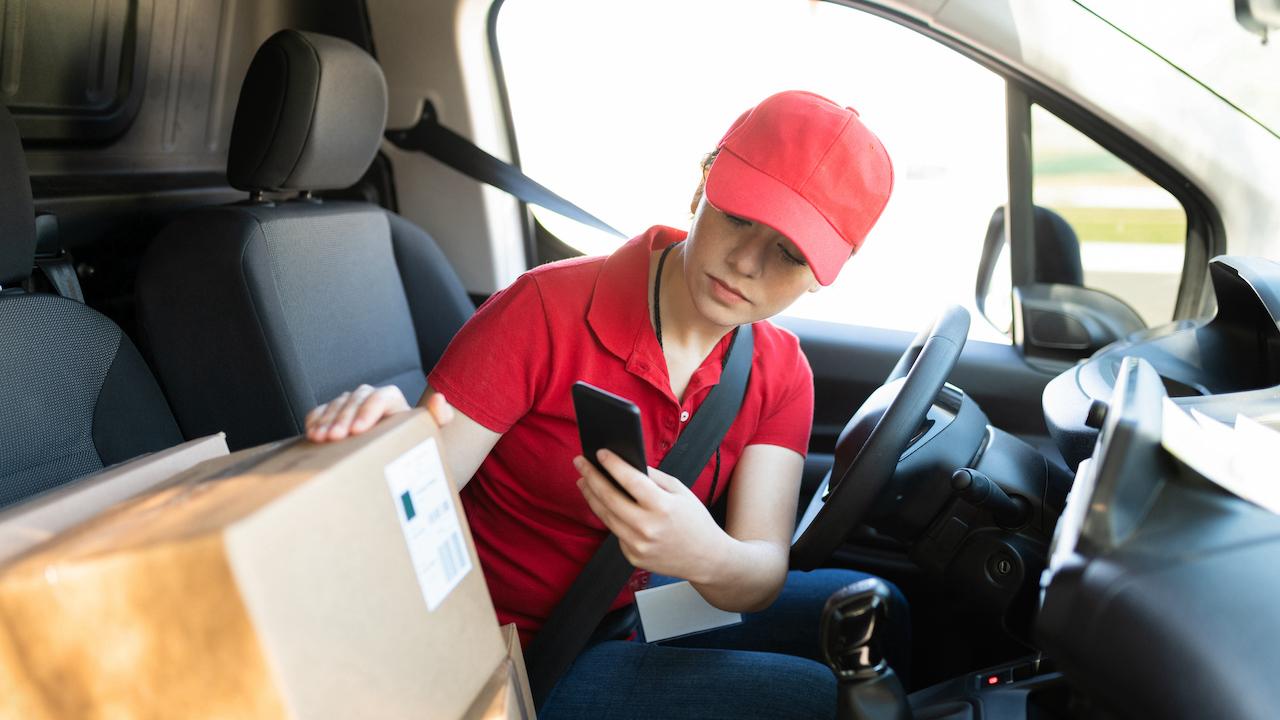 Delivery driver in a van checking a smartphone next to a labeled parcel