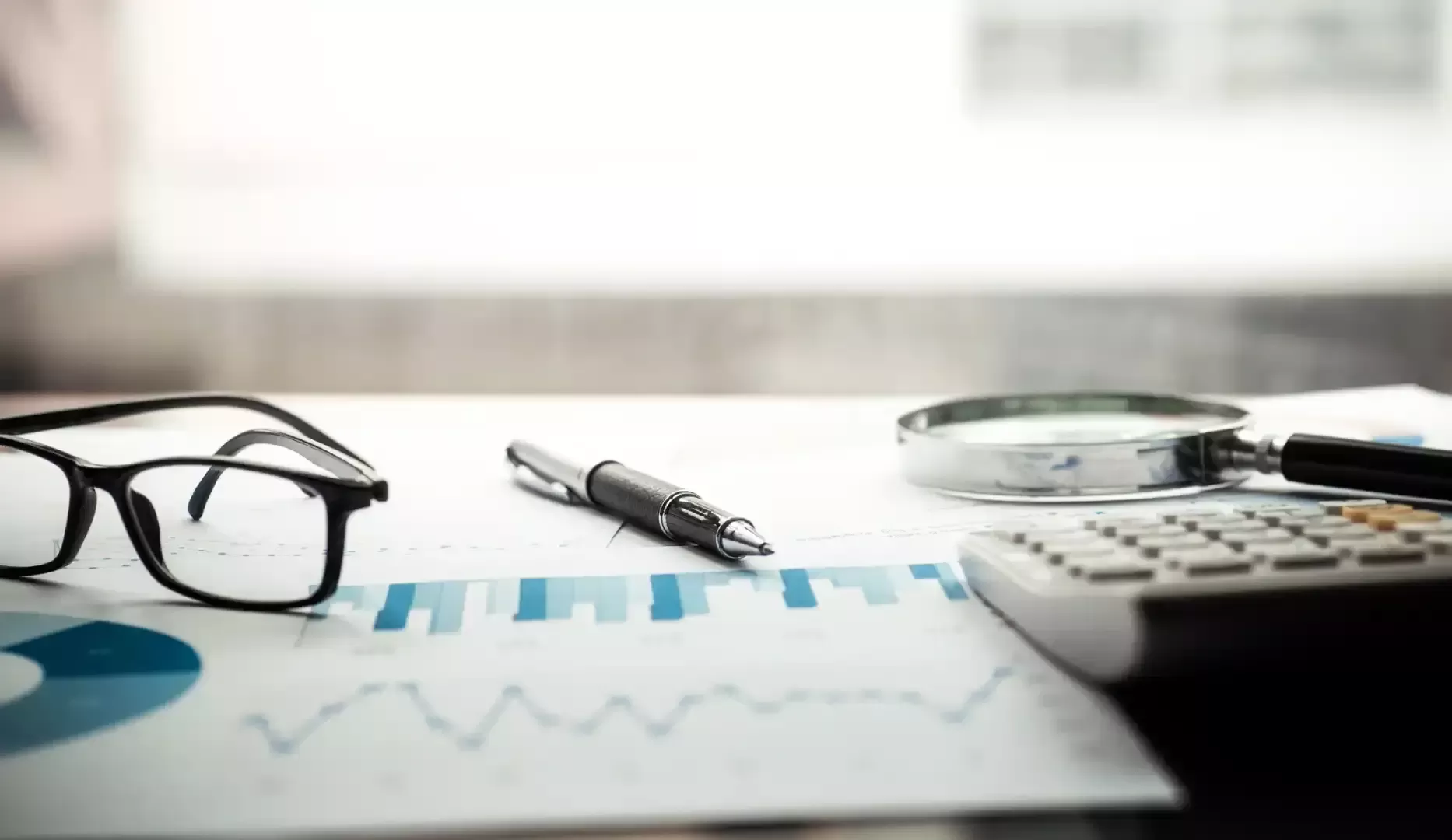 Charts, glasses, pen, magnifier and calculator on a desk for a performance analysis