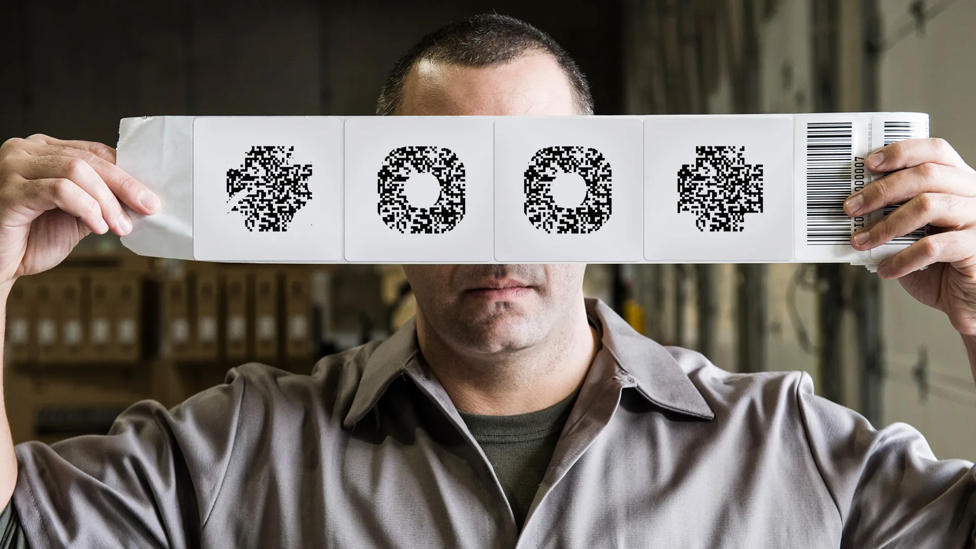 Worker holding up a strip of labels with damaged 2D codes and a linear barcode