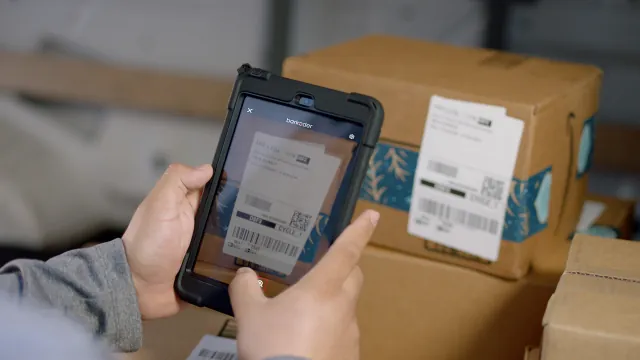 Tablet running barKoder scanning a shipping label barcode on a cardboard box